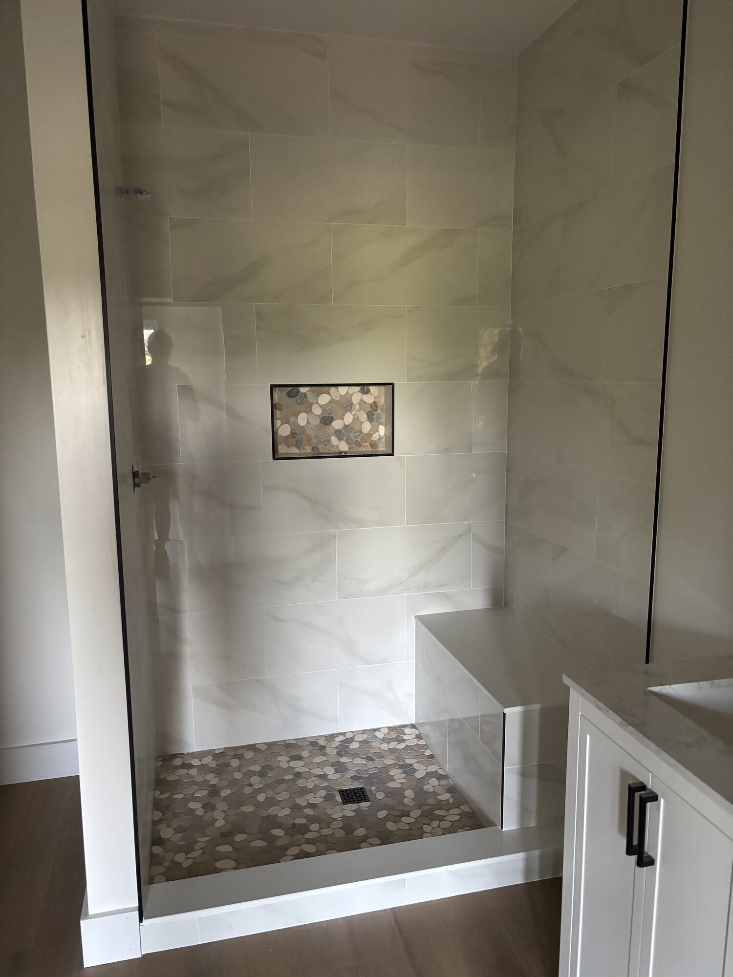 Marble walk-in shower with custom pebble mosaic floor and matching niche, built-in bench