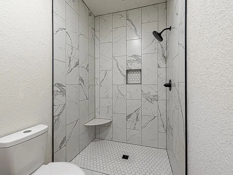 Marble vertical-stack tile shower with hexagon mosaic floor, corner bench, and matte black fixtures